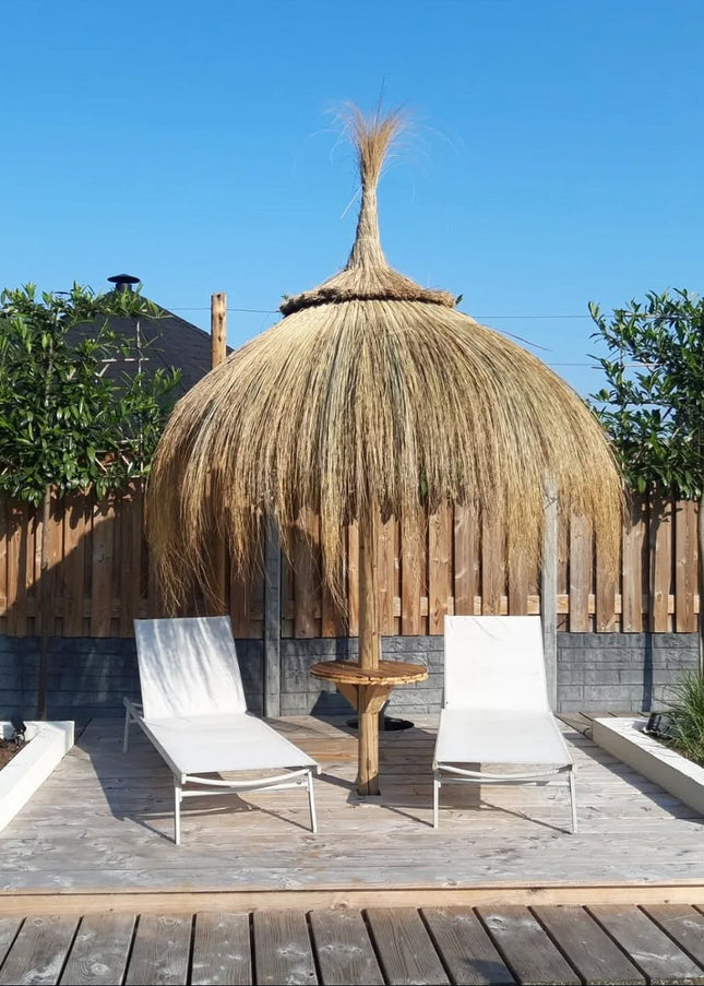 Luxe rieten parasol 220 cm met stevig metalen frame en houten paal, handgemaakt in Spanje, geplaatst in een tuin voor een exotische sfeer.